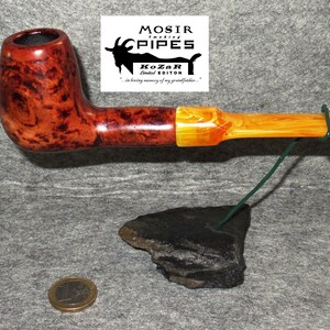 May include: A brown and orange wooden pipe with a black bowl and a yellow acrylic stem. The pipe is on a black rock stand with a green wire.
