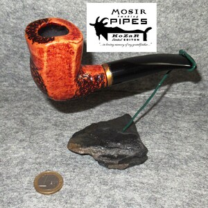 Peut inclure: Une pipe à fumer brune et noire avec une bande dorée. La pipe est sur un support en pierre noire avec un fil vert.