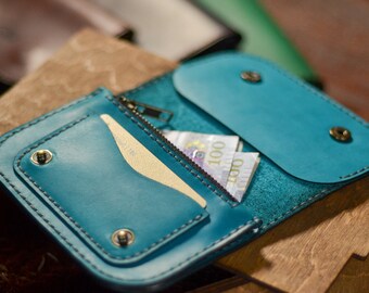 May include: A teal leather wallet with a zipper closure and two snap buttons. The wallet is open and has cash inside.