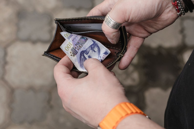 Op de afbeelding: Een bruine leren portemonnee met een ritssluiting is open en toont een Tsjechisch bankbiljet van 100 kronen.