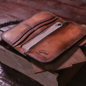 May include: A brown leather wallet with a chain attached. The wallet is open and has a zippered pocket and multiple card slots. The wallet is embossed with the text "Greesh Handmade in Georgia".
