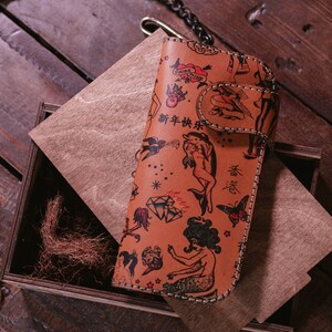 May include: A brown leather wallet with a colorful tattoo-style design. The wallet features images of mermaids, dolphins, butterflies, and other traditional tattoo imagery. The text "新年快乐" is printed on the wallet.