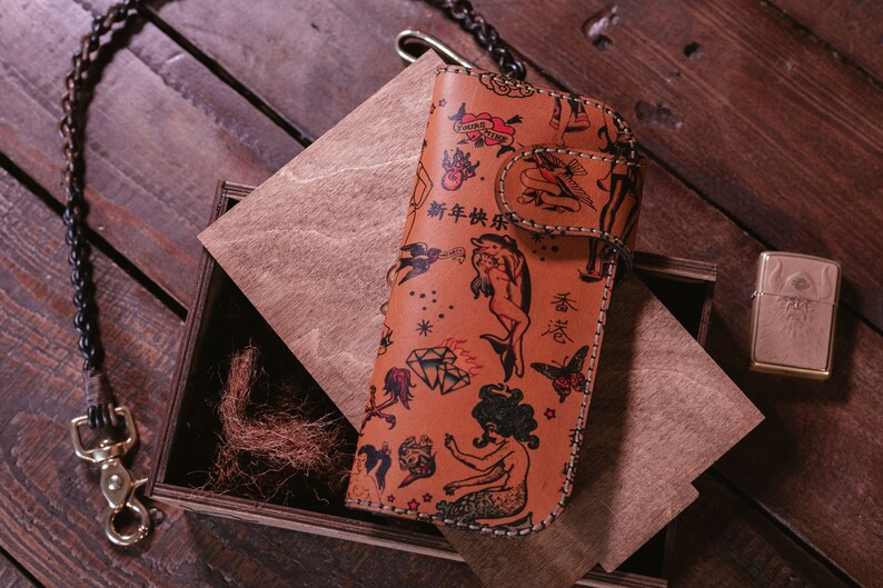 May include: A brown leather wallet with a colorful tattoo-style design. The wallet features images of mermaids, dolphins, butterflies, and other traditional tattoo imagery. The text "新年快乐" is printed on the wallet.