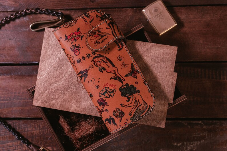May include: A brown leather wallet with a stitched border and a variety of colorful tattoo-style illustrations, including a mermaid, a bird, a heart, and a diamond. The wallet has the text "新年快乐" and "福" printed on it.