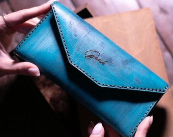 May include: A teal blue leather wallet with a flap closure and the word "Gresh" embossed on the front.