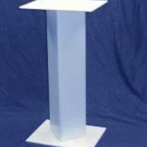 May include: White pedestal stand with a rectangular top and a square base. The stand is made of a smooth, white material.