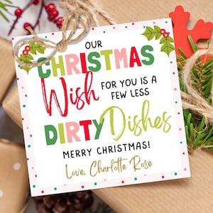 May include: Christmas gift tags with the text "Our Christmas Wish for you is a few less dirty dishes". The tags are on wrapped gifts with red snowflake and holly accents. Greenery and pinecones are also present.