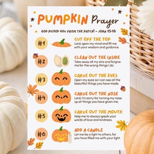 Puede incluir: Una naturaleza muerta con calabazas blancas, una cesta decorativa con flores blancas y una tarjeta de "Pumpkin Prayer". La tarjeta tiene ilustraciones de calabazas y texto. También hay una calabaza naranja y hojas de otoño.