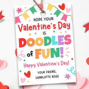 May include: A Valentine's Day gift tag with the message "Hope Your Valentine's Day is Doodles of Fun!" in colorful letters. The tag is decorated with hearts, banners, and a gold string. Red and pink paper hearts and ribbon are scattered around the tag.