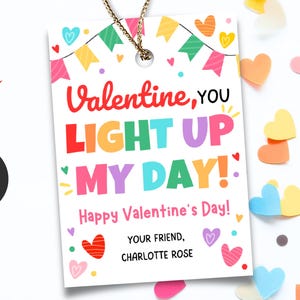 Op de afbeelding: Een Valentijnsdag cadeaulabel met de tekst "Valentine, YOU LIGHT UP MY DAY!" in kleurrijke letters. Het label heeft een gouden touwtje en is versierd met hartjes en een banner. De woorden "Happy Valentine's Day!" en de naam "CHARLOTTE ROSE" zijn ook opgenomen.