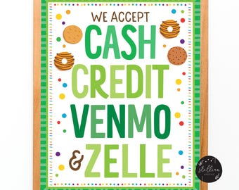 May include: A framed sign with a wooden border, displaying the text "WE ACCEPT CASH CREDIT VENMO & ZELLE" in green. The sign is decorated with colorful confetti and cookie illustrations. A small black circle with white text is in the bottom right corner.