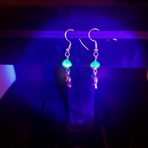 May include: A pair of silver dangle earrings with green faceted glass beads. The earrings are hanging from a black surface.