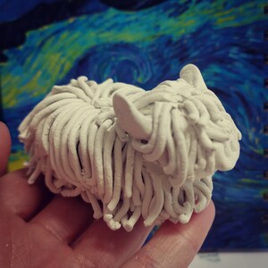 May include: A white clay sculpture of a dog with long, shaggy hair. The sculpture is made of individual strands of clay that are twisted and intertwined to create the effect of fur.