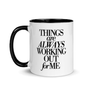 May include: White ceramic coffee mug with a black rim and handle. The mug has black text that reads "Things are always working out for me."