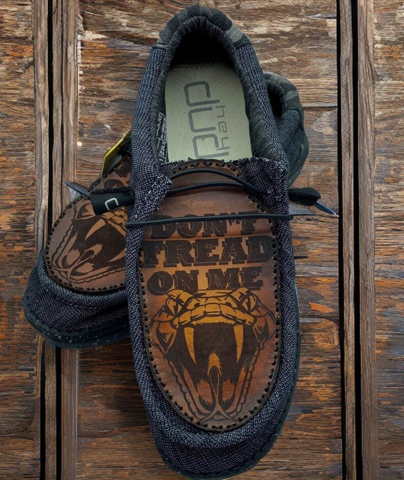 May include: A pair of black canvas shoes with brown leather accents. The shoes feature a snake graphic and the text "Don't Tread On Me".
