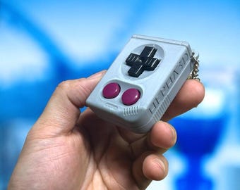 May include: A gray and black miniature video game controller keychain with purple buttons. The keychain has the text "PHASE 3D" printed on the side.