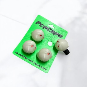 May include: Four white 3D-printed tyre valve caps with red accents and a black valve stem, displayed on a green card. The card has the text "POP CAPS" and "3D PRINTED TIRE VALVE CAPS".