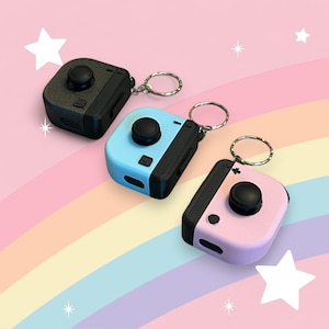 Puede incluir: Tres juguetes de fidget con llavero en negro, azul y rosa. Cada juguete tiene una perilla redonda giratoria y un botón pequeño. Los llaveros están unidos a anillos plateados.