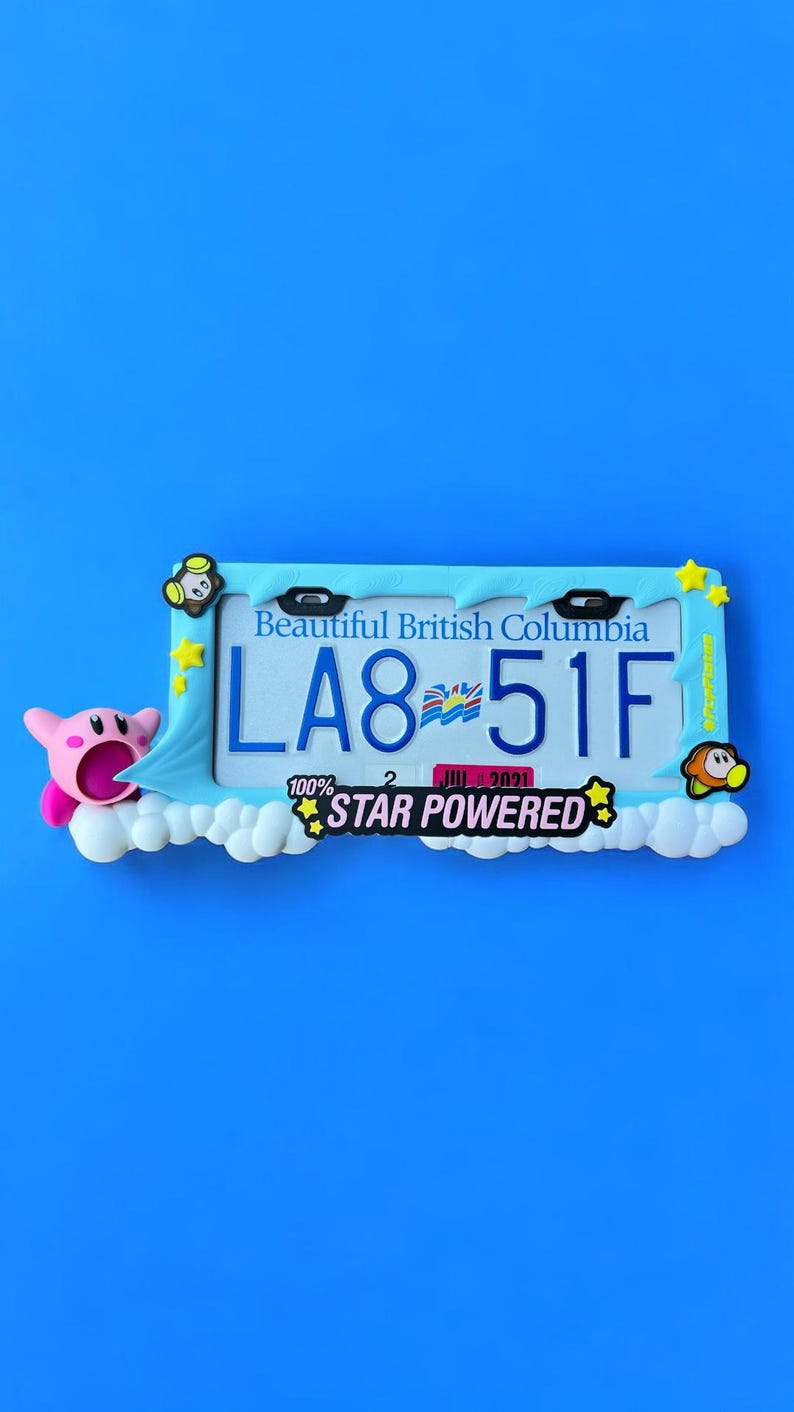 May include: A decorative license plate frame with a blue border and the text "Beautiful British Columbia". The plate reads "LA8-51F" with a cartoon character and the words "STAR POWERED". The frame is on a blue background.