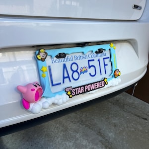 May include: A light blue license plate frame with the text "Beautiful British Columbia" and a license plate that reads "LA8 51F". The frame is decorated with cartoon characters and the words "100% STAR POWERED".