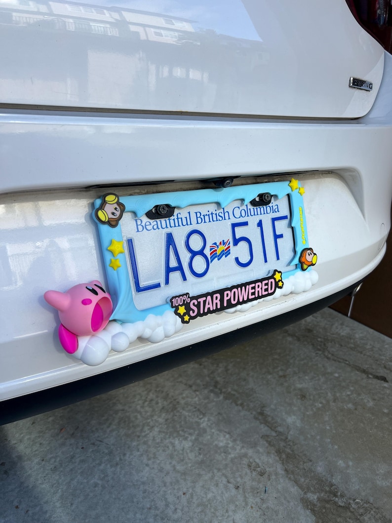 May include: A light blue license plate frame with the text "Beautiful British Columbia" and a license plate that reads "LA8 51F". The frame is decorated with cartoon characters and the words "100% STAR POWERED".