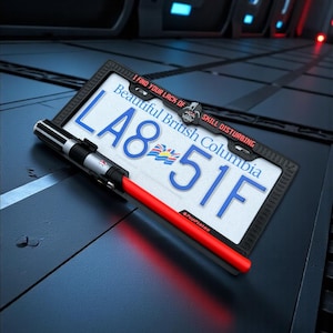 May include: A license plate frame with a British Columbia license plate and a red lightsaber prop. The license plate reads "LA8 51F" and "Beautiful British Columbia". The frame has the text "I FIND YOUR LACK OF SKILL DISTURBING".