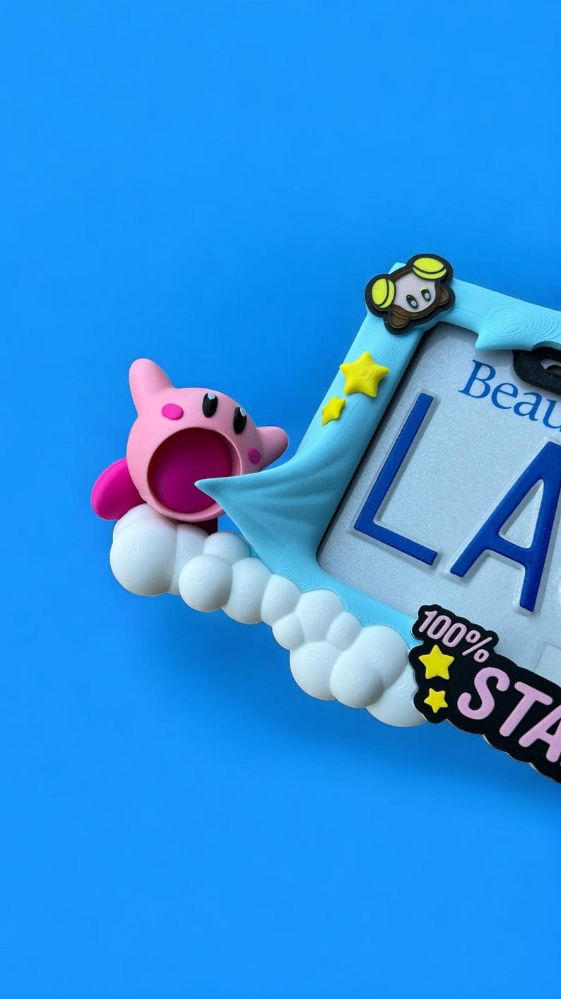 May include: A light blue picture frame with a cartoon character and the text "LA". The frame has a cloud and star design, with the words "100% STA" on the bottom right. The background is a solid blue.