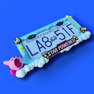 May include: A blue license plate frame with the text "Beautiful British Columbia" and the license plate number "LA8 51F". The frame is decorated with a cartoon character and the words "100% STAR POWERED".
