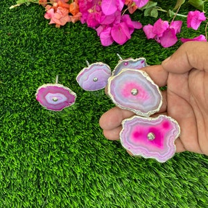 May include: Five pink and white agate drawer pulls with silver trim. The pulls are on a green artificial grass background.