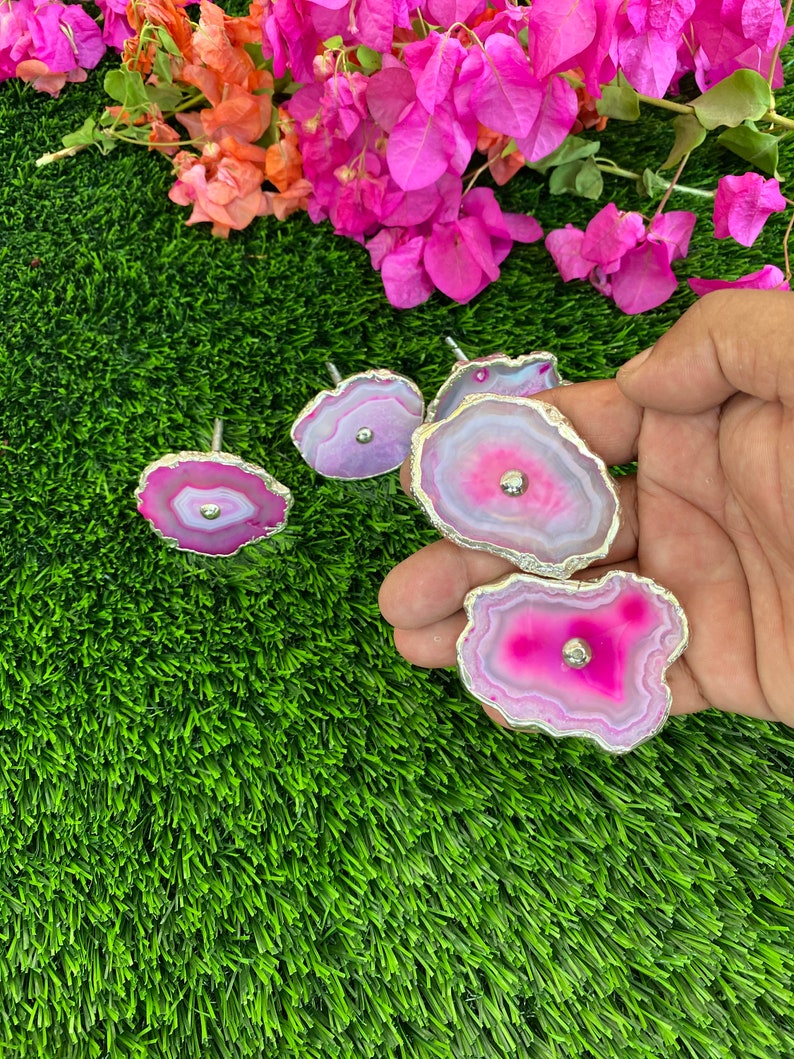 May include: Five pink and white agate drawer pulls with silver trim. The pulls are on a green artificial grass background.