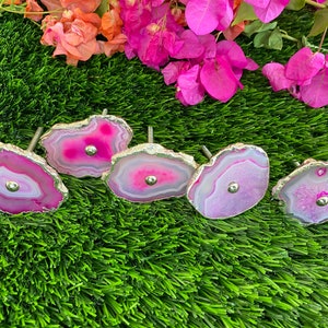 May include: Five pink agate drawer pulls with silver metal accents. The pulls are arranged on a green artificial grass surface.