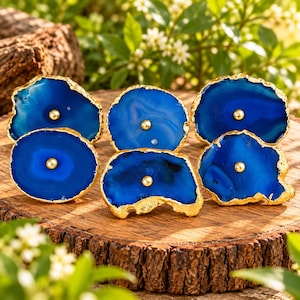 May include: A set of six blue agate stone cabinet knobs with irregular, organic shapes and natural banding. Each slice features a polished, vibrant blue surface with a metallic gold-tone rim and a centred gold-tone metal knob hardware.