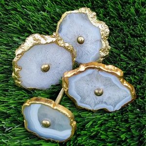 May include: Three white agate drawer pulls with gold trim. The pulls are shaped like irregular circles with a gold screw in the center.