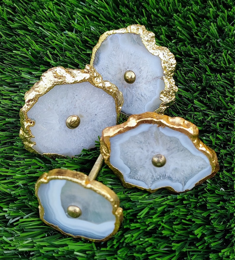 May include: Three white agate drawer pulls with gold trim. The pulls are shaped like irregular circles with a gold screw in the center.