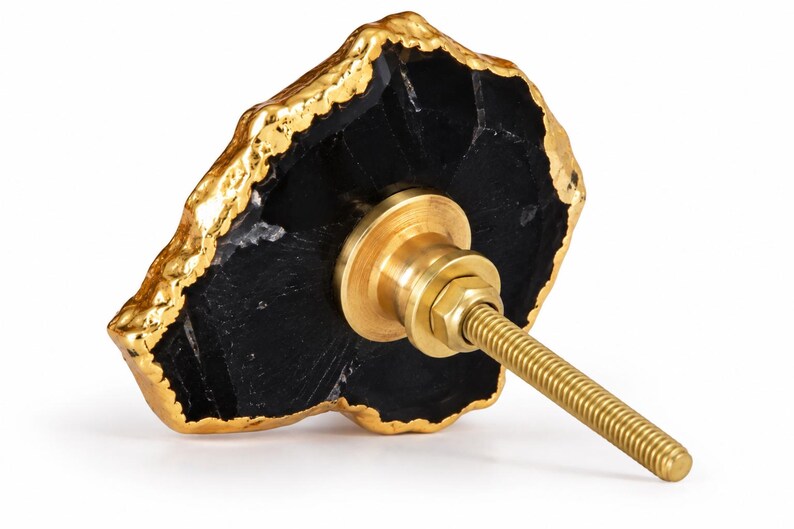 May include: A cabinet knob featuring a slice of black stone with a textured, metallic gold-colored edge. The back of the knob includes a brass-toned metal mounting base with a threaded bolt extending outward for installation on furniture or doors.