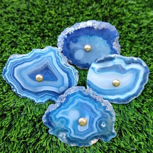 Puede incluir: Cuatro rebanadas de ágata azul con detalles dorados. Las rebanadas de ágata tienen una forma natural y orgánica y son perfectas para agregar un toque de naturaleza a la decoración de tu hogar.