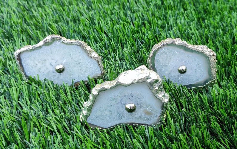 May include: Three white agate drawer pulls with silver metal trim. The pulls are shaped like irregular ovals with a smooth, polished surface.