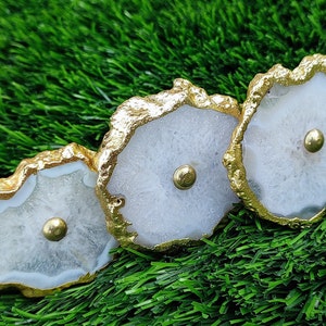 May include: Three white agate drawer pulls with gold trim. Each pull has a round, gold knob in the center.