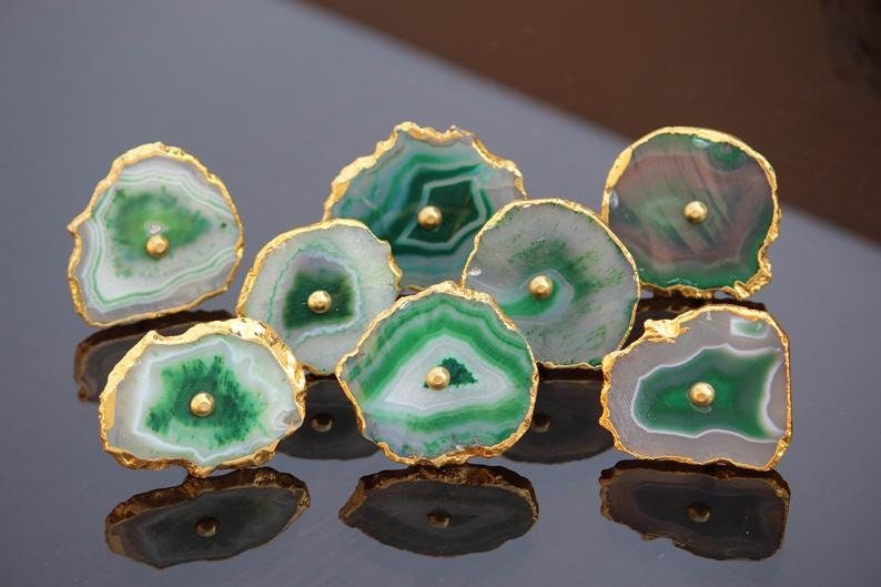 May include: A set of seven green agate drawer pulls with gold trim. Each pull features a unique pattern of green and white agate with a gold dot in the center.
