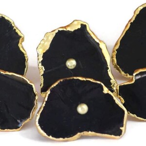 May include: A set of five irregular, black, stone-like cabinet knobs with gold-toned metallic edges. Each knob features a smooth, glossy black surface with a single, centered, small, round, gold-toned metal stud detail on the front face.