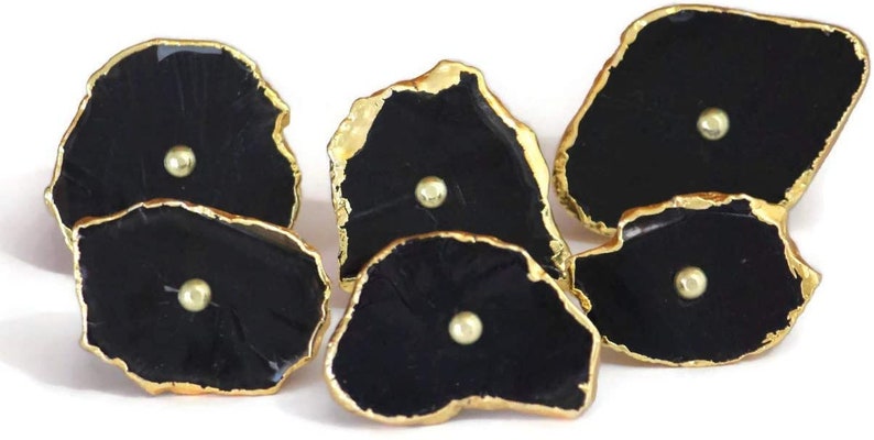 May include: A set of five irregular, black, stone-like cabinet knobs with gold-toned metallic edges. Each knob features a smooth, glossy black surface with a single, centered, small, round, gold-toned metal stud detail on the front face.