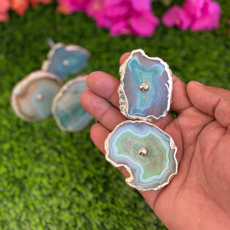 May include: Two agate drawer pulls with silver metal accents. The agate is green, blue, and white with a swirling pattern. The pulls have a round metal knob in the center.