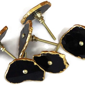 May include: A collection of five cabinet knobs featuring irregular, flat black stone-like faces with metallic gold-painted edges. Each knob includes a central silver-toned metal screw post with a washer and nut for mounting purposes.