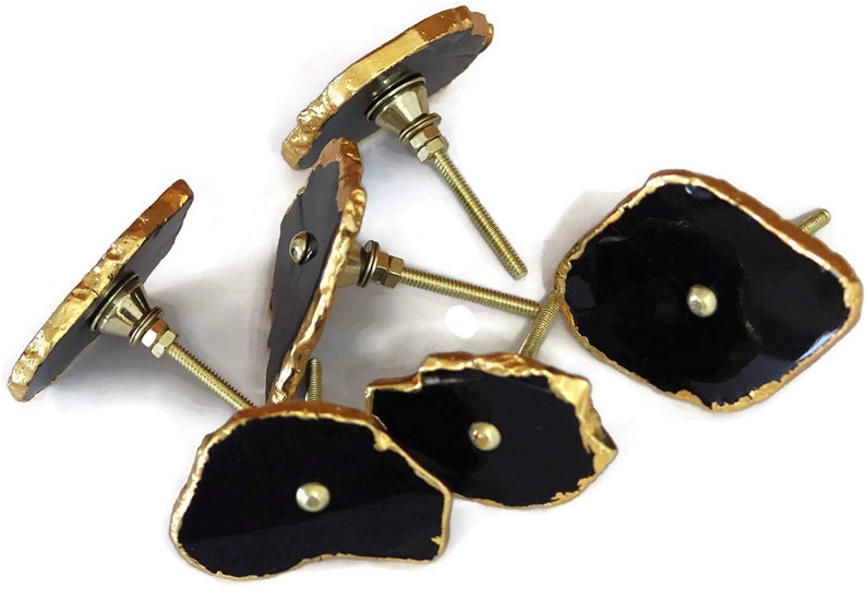 May include: A collection of five cabinet knobs featuring irregular, flat black stone-like faces with metallic gold-painted edges. Each knob includes a central silver-toned metal screw post with a washer and nut for mounting purposes.