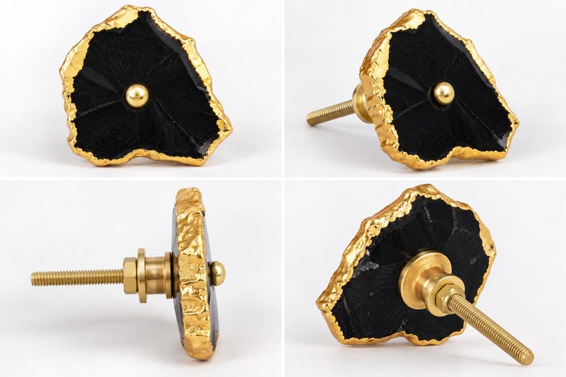 May include: A cabinet knob featuring a flat, irregular black stone face with a textured, metallic gold-colored edge. A small gold-colored metal sphere is centered on the front, and a threaded gold-colored metal bolt extends from the back.