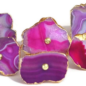 May include: Six agate drawer pulls with gold trim. Each pull features a different pattern of pink, purple, and white agate.