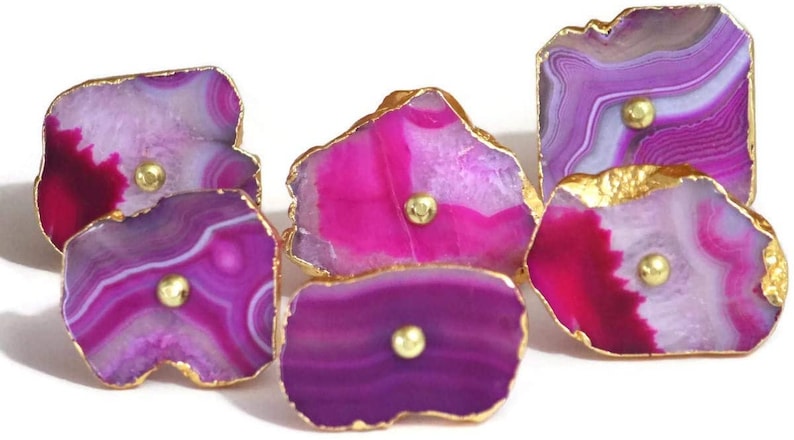 May include: Six agate drawer pulls with gold trim. Each pull features a different pattern of pink, purple, and white agate.