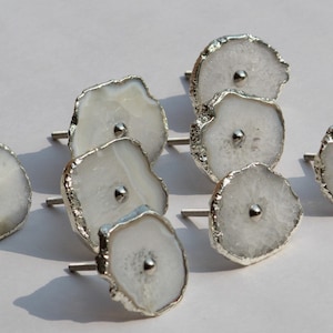 May include: A set of eight white agate drawer pulls with silver accents. Each pull has a unique shape and features a small silver knob in the center.