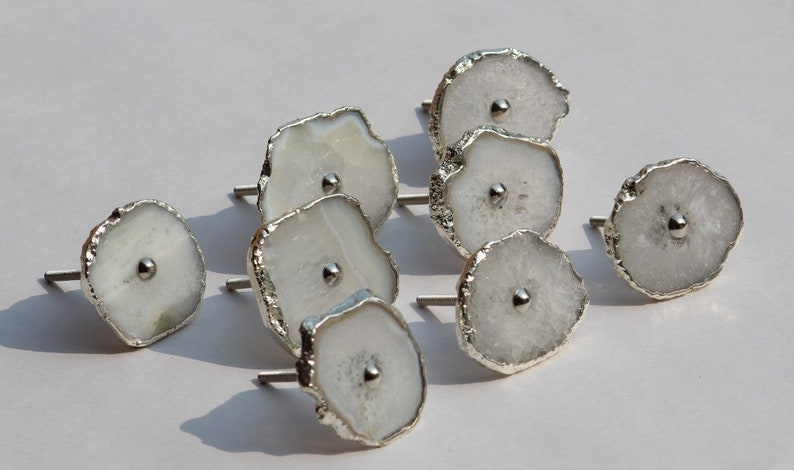 May include: A set of eight white agate drawer pulls with silver accents. Each pull has a unique shape and features a small silver knob in the center.