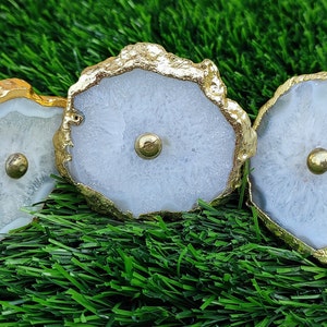May include: Three white agate knobs with gold trim. The knobs have a round shape and a small gold knob in the center.